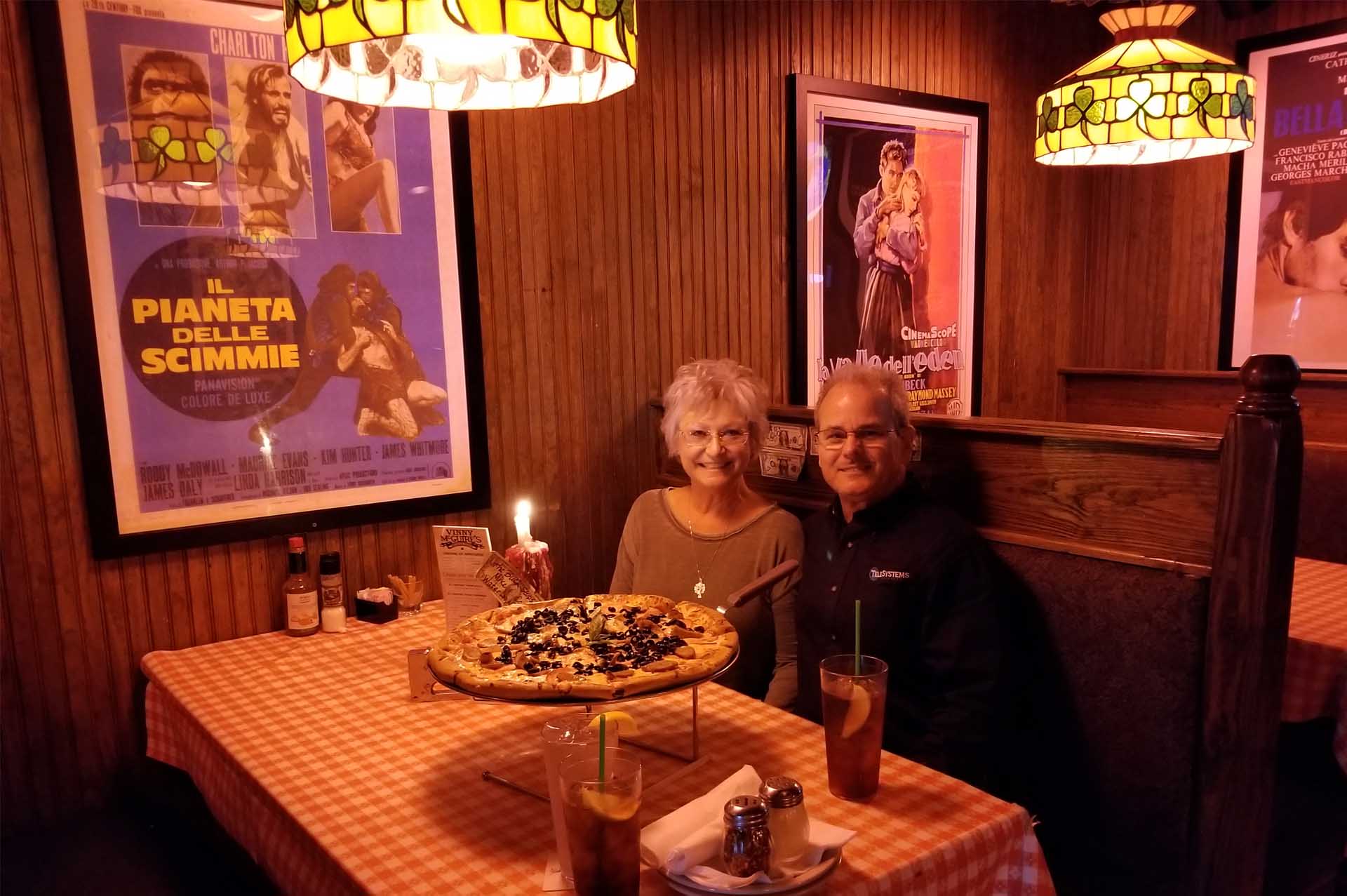 smiling couple sitting at restaurant table with large pizza in front of them